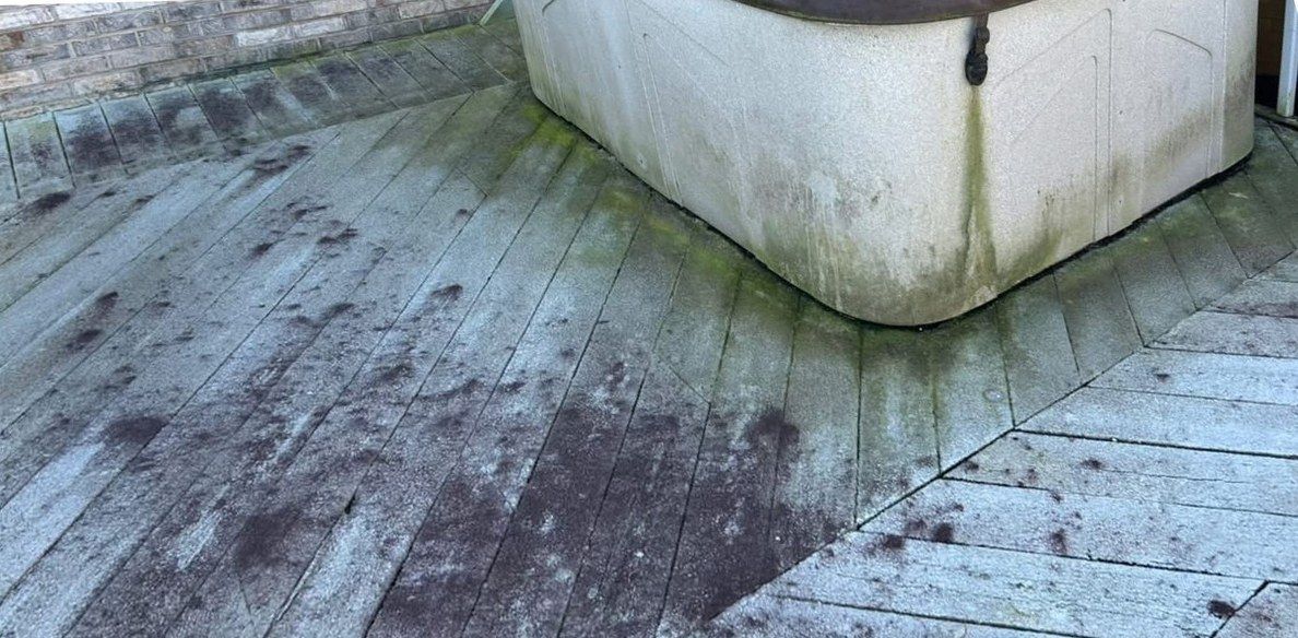 Composite deck boards around a hot tub, gray and spotted with green and black growth