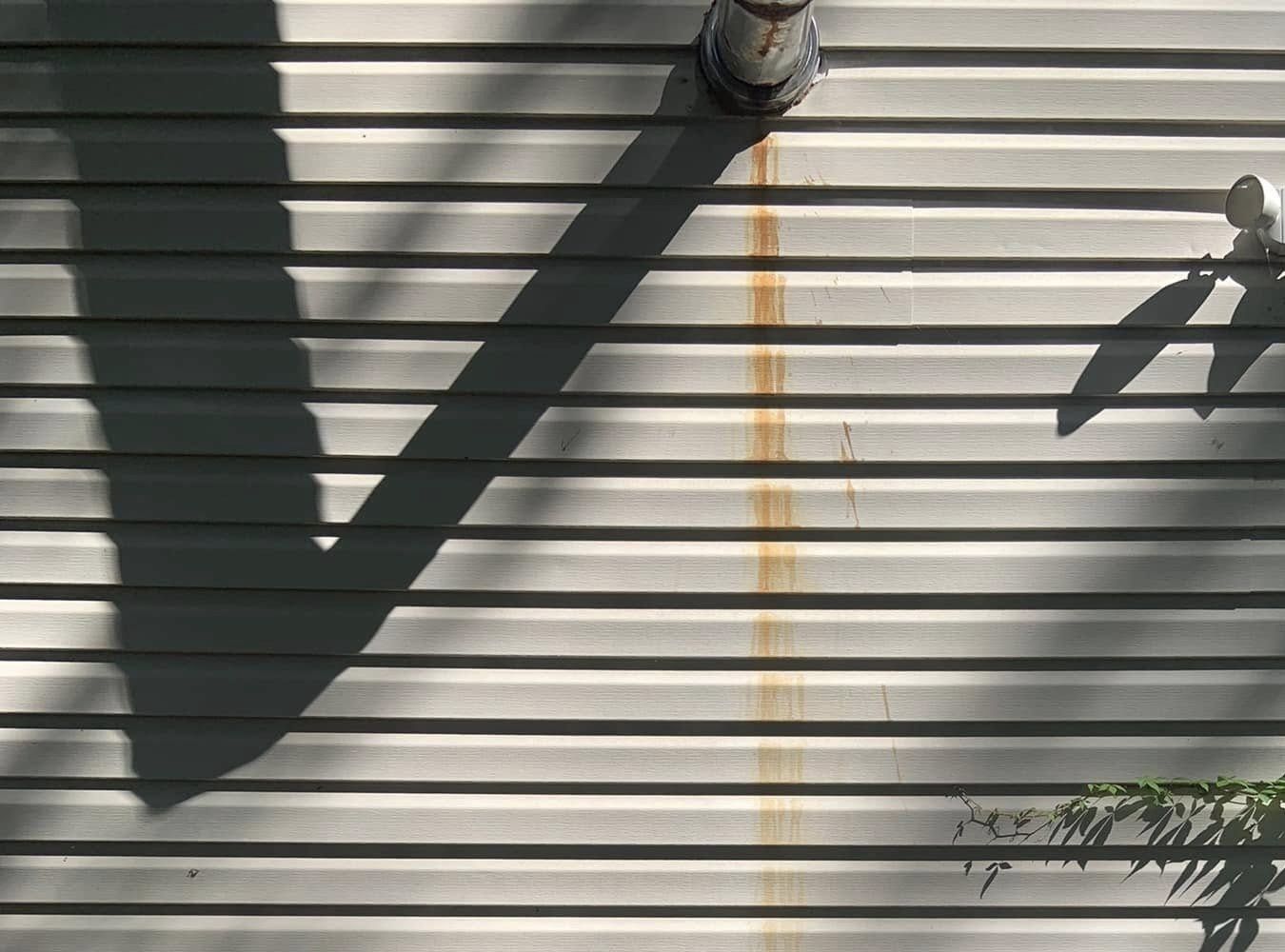 Orange rust streak running down vinyl siding below a vent pipe