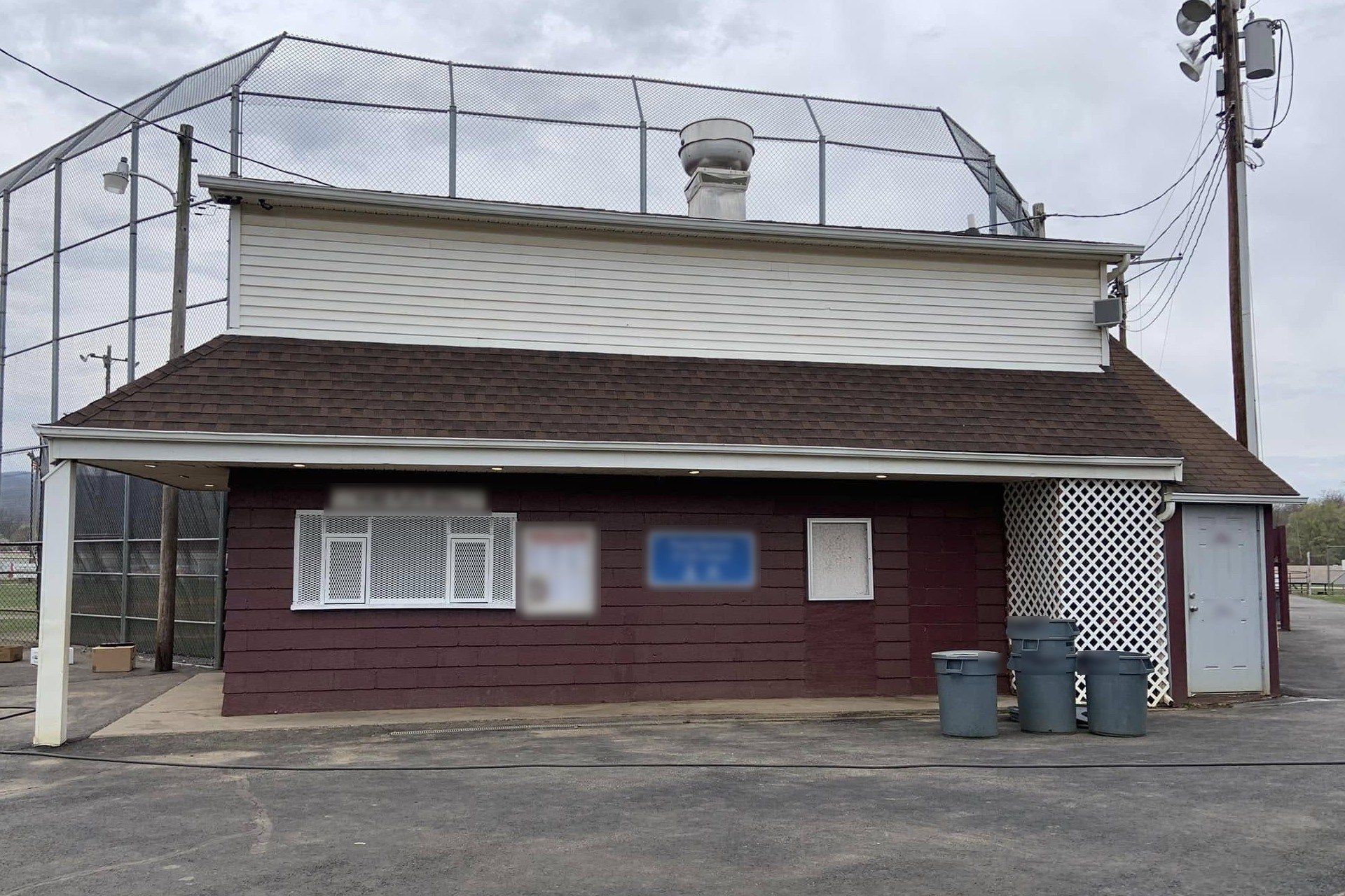 Concession stand with maroon siding and white trim beside a Front Royal ballfield backstop, after a wash