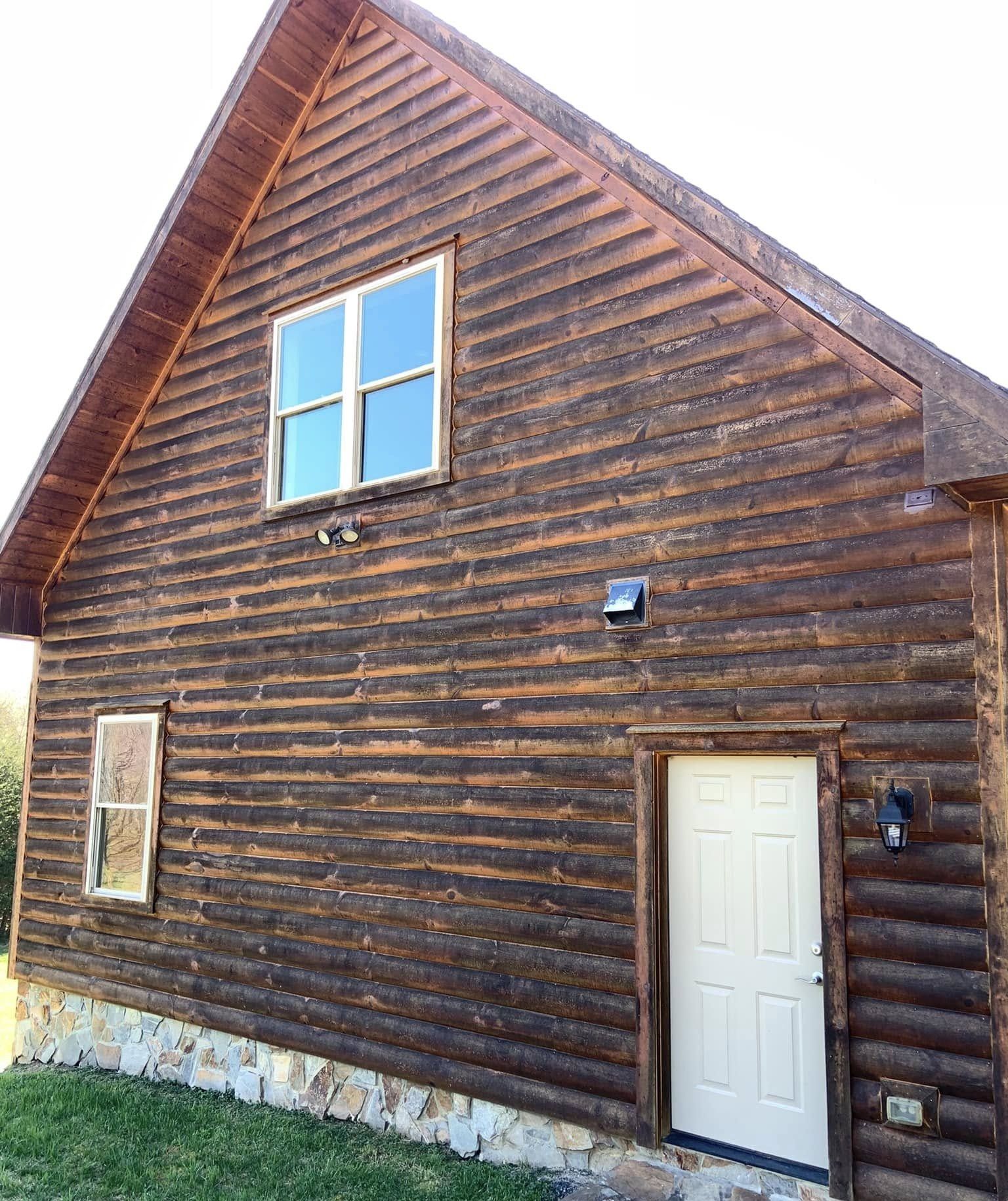 Log-sided gable wall with dark, blotchy weathering above a stone foundation