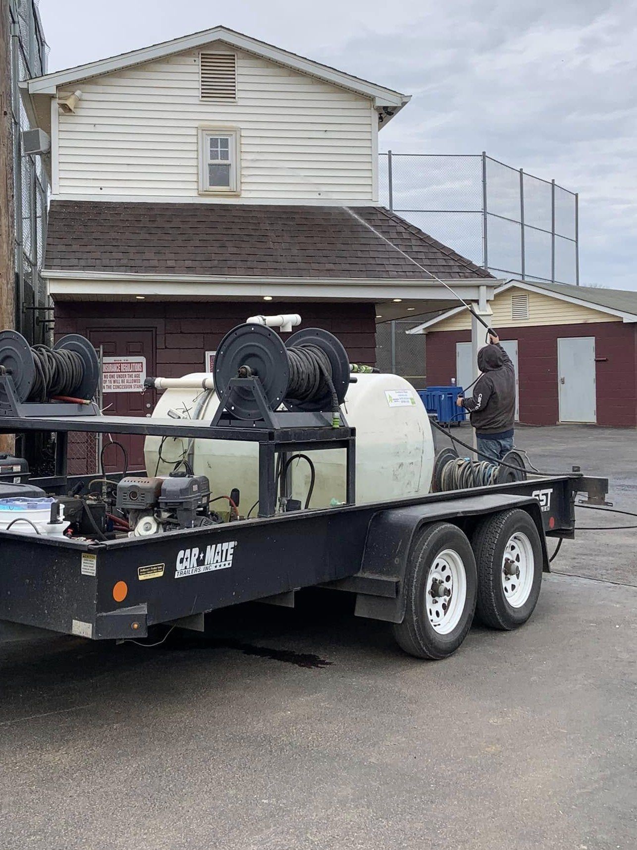 Chem-Clean trailer with water tank and hose reels parked beside a two-story building while a crew member reaches a long wand up to the roofline