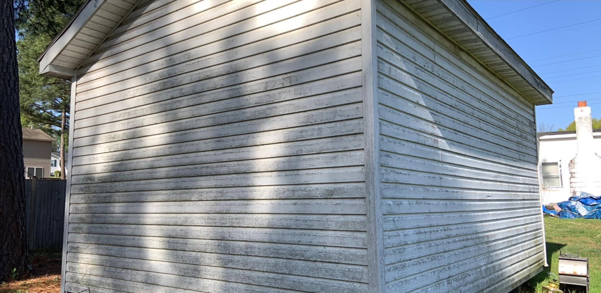 Corner of a white vinyl shed, both walls gray and streaked with mildew