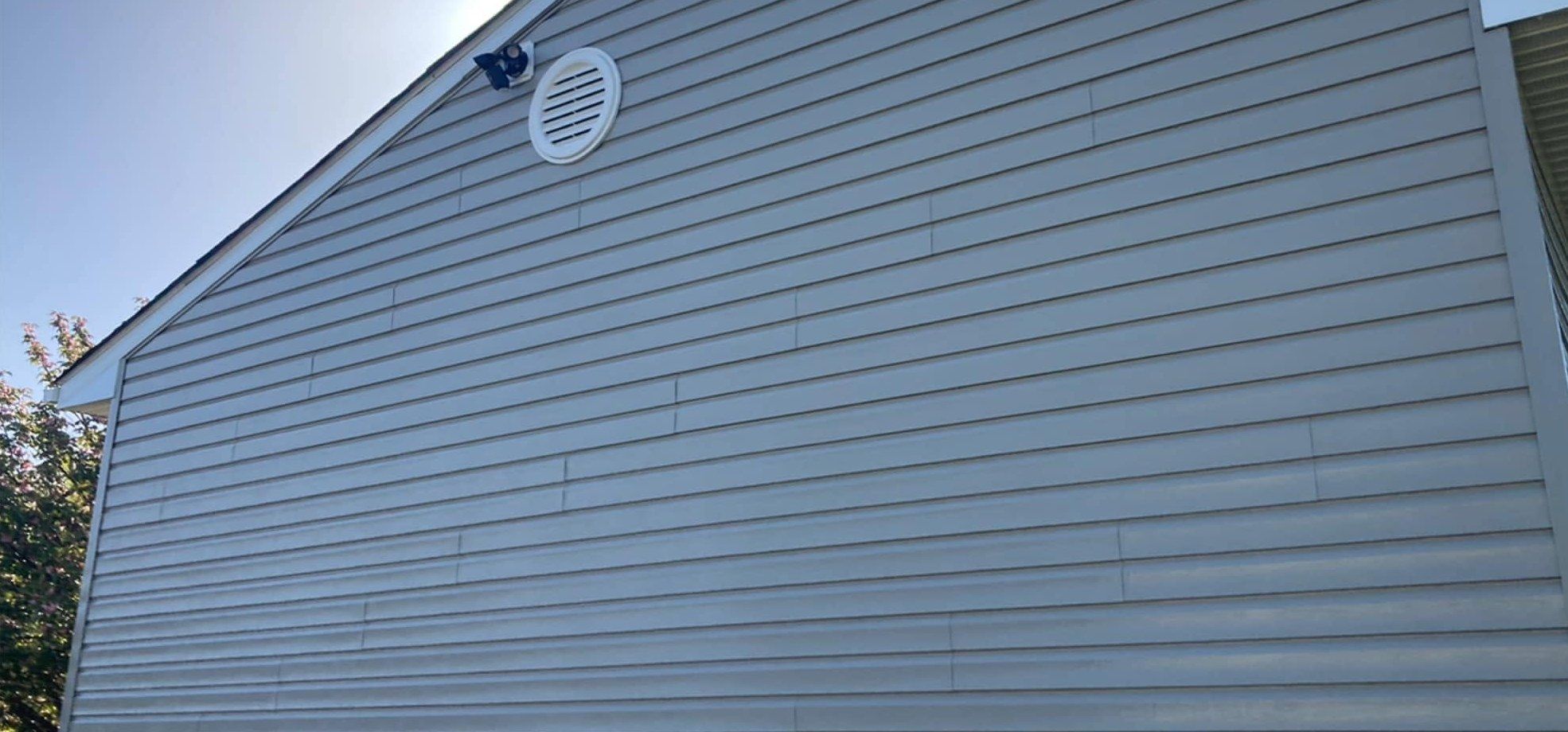 The same gable after washing, clean even gray siding below the vent