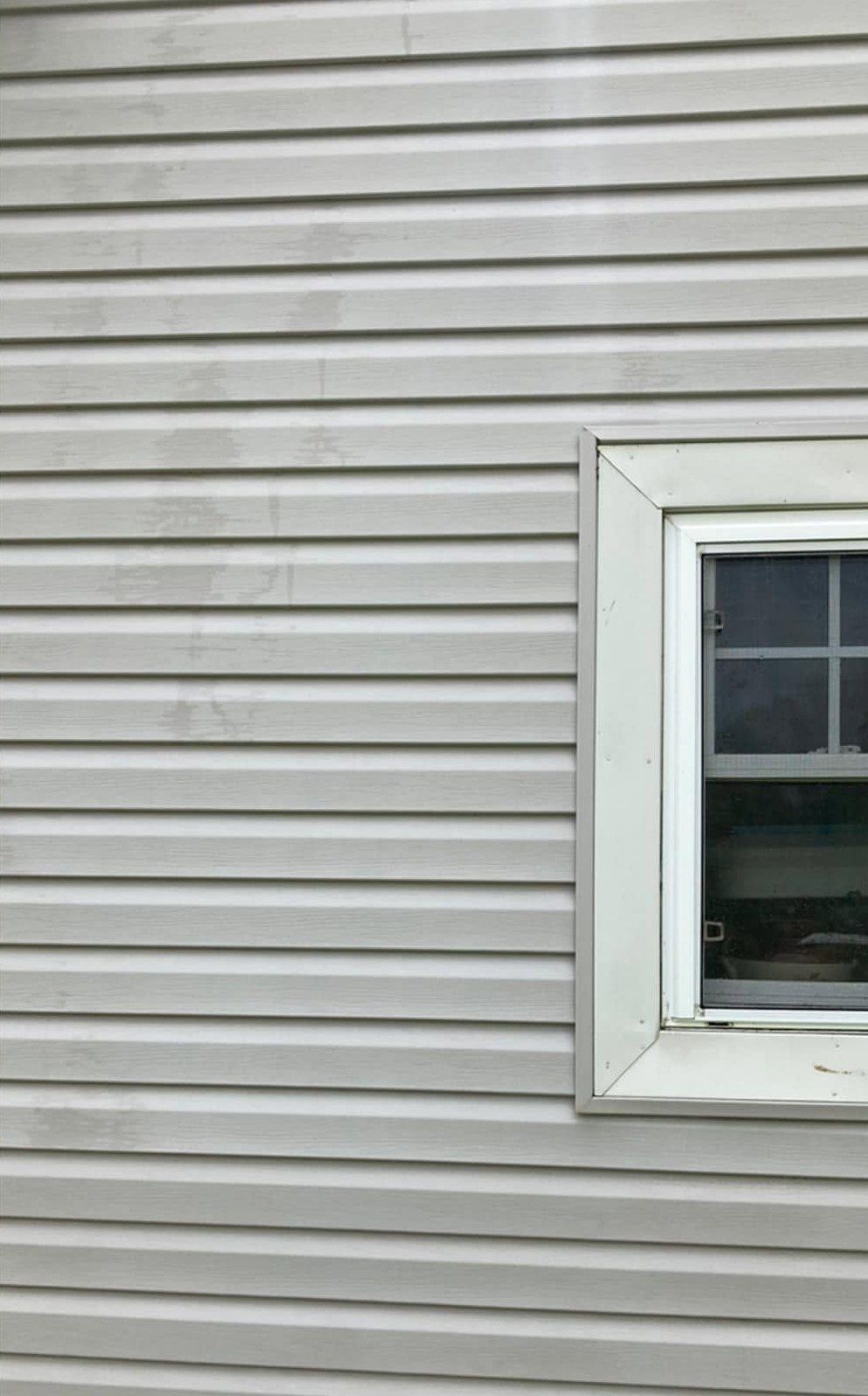 The same siding after washing, clean white laps beside the window trim