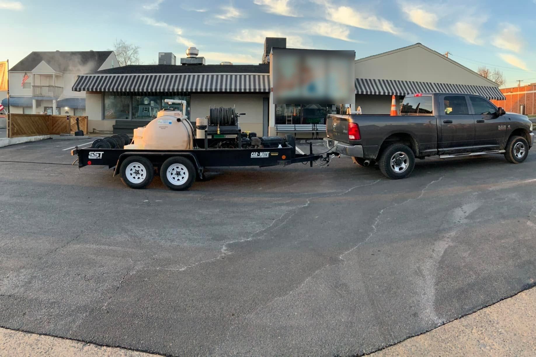 Pickup towing a water-tank pressure-washing trailer in a commercial parking lot at sunrise