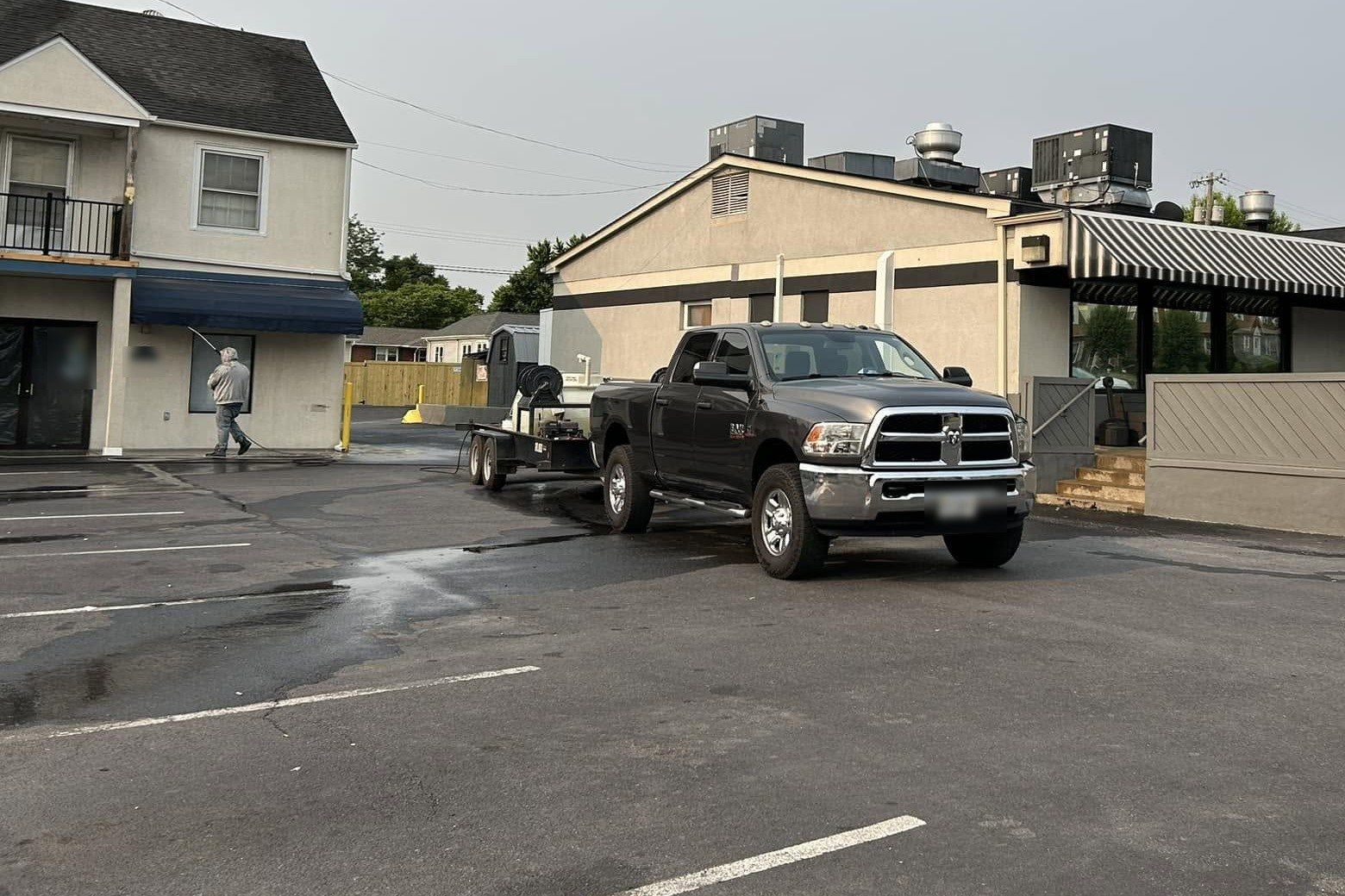 Crew member washing a commercial building wall with the pressure-washing truck and trailer parked nearby