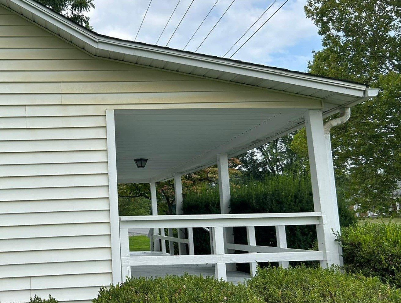 White vinyl siding beside a covered porch, yellow-green grime under the eave before washing