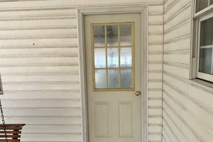 Covered porch door and white siding with dark dirt lines along each lap before washing