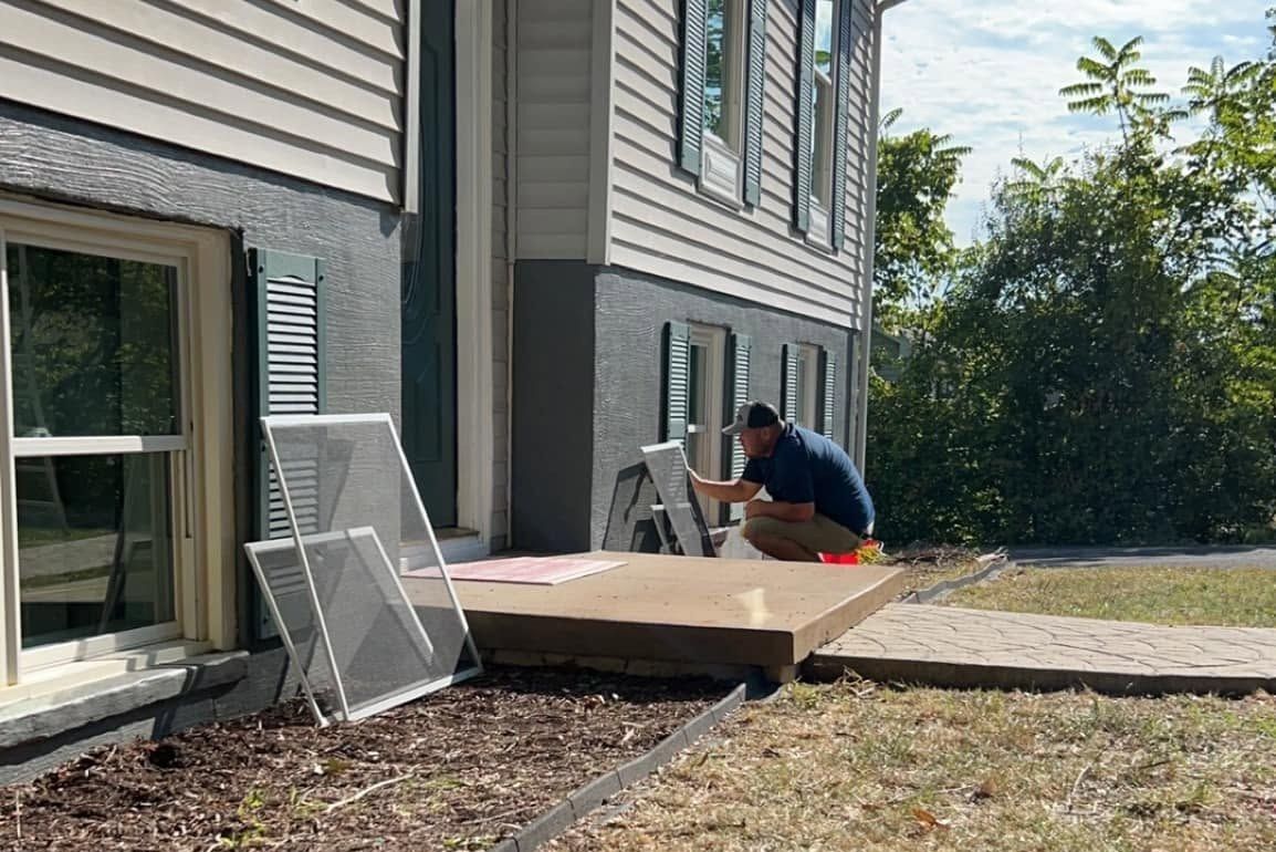 Crew member cleaning window screens on the front stoop during a house wash