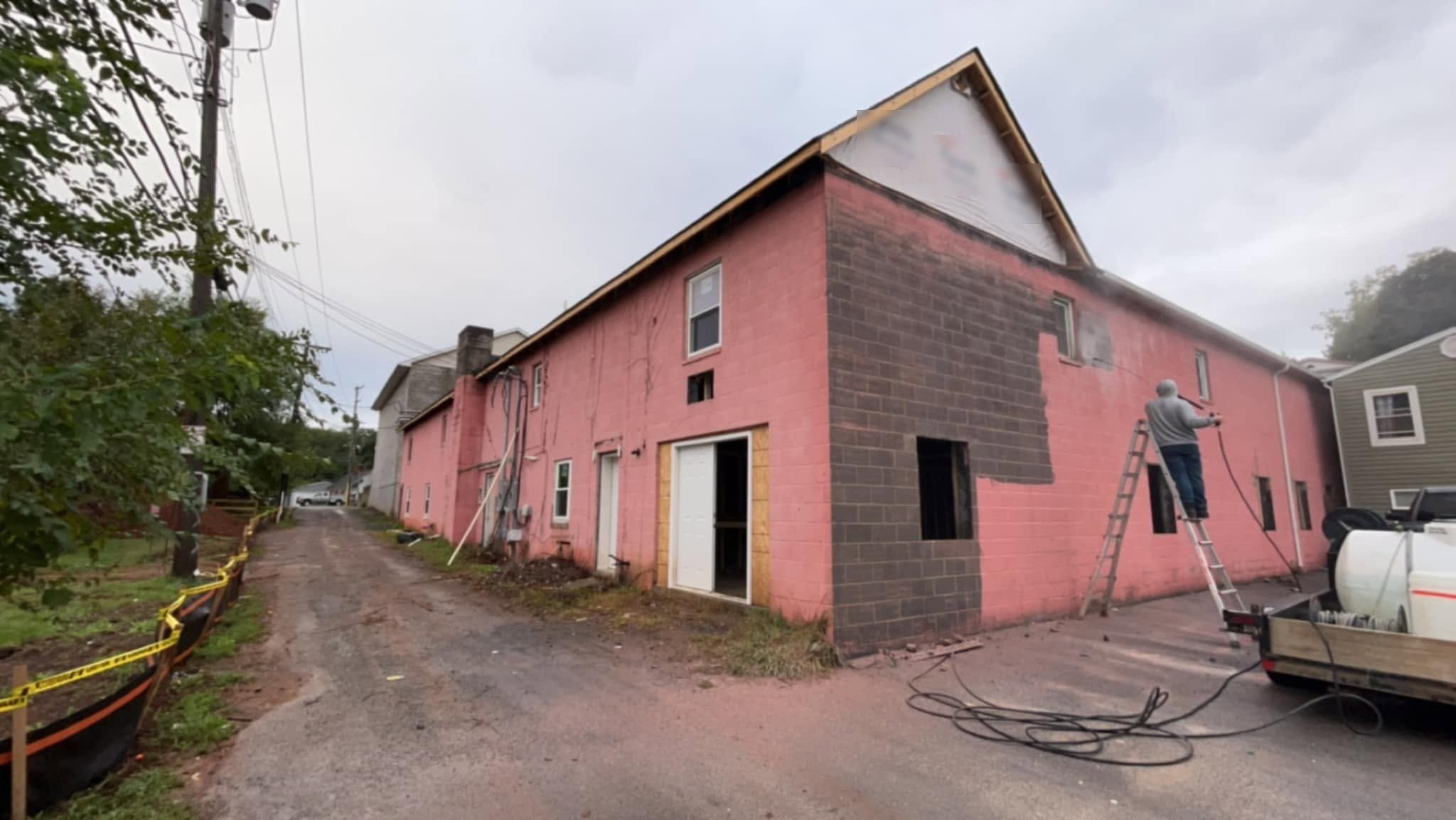 Block wall partway through washing, pink paint showing where grime is gone and a dark patch still to do