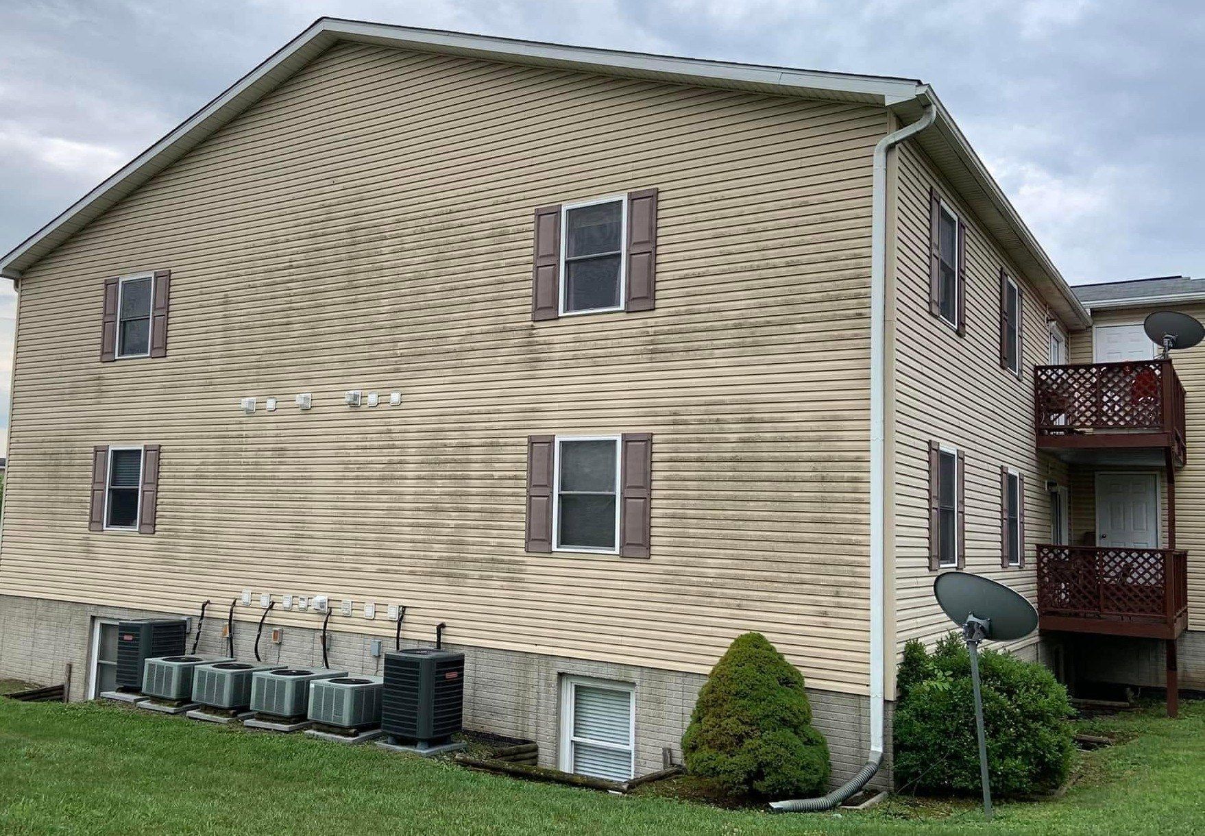 Dark mildew streaks across the tan siding of a three-story apartment building