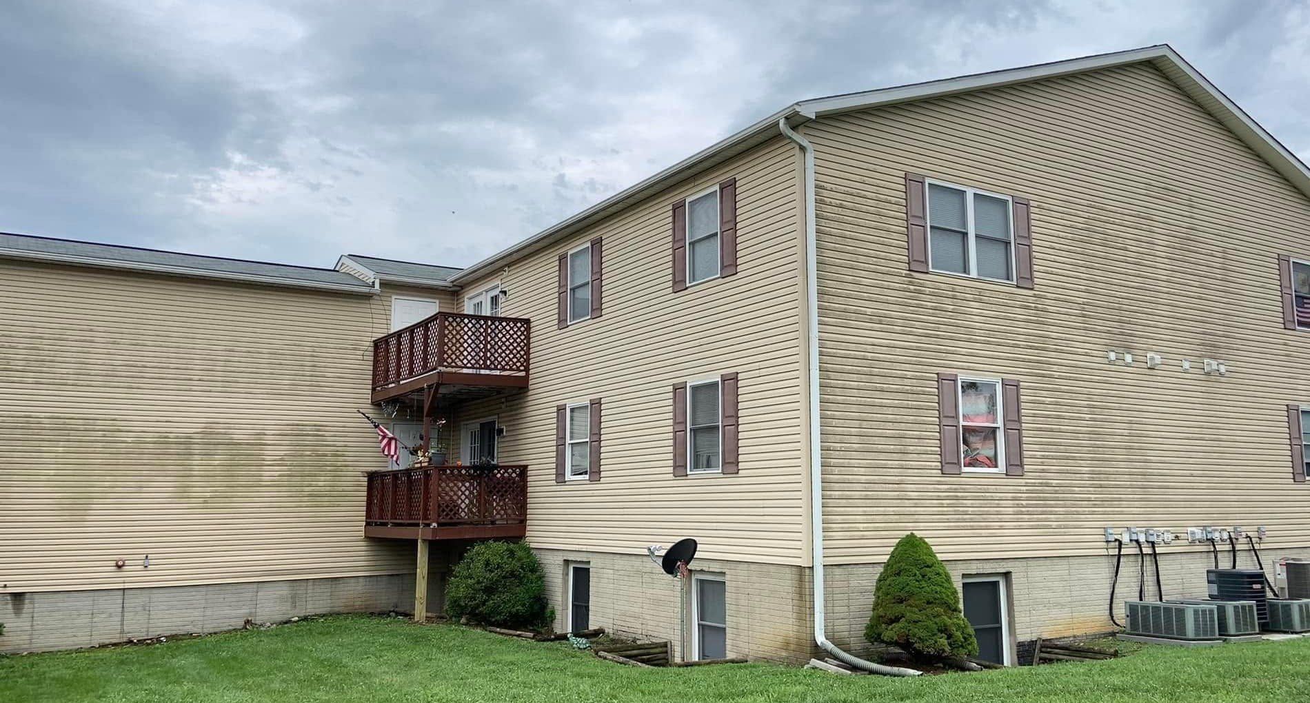 Green mildew streaks across tan vinyl siding on a multi-unit building