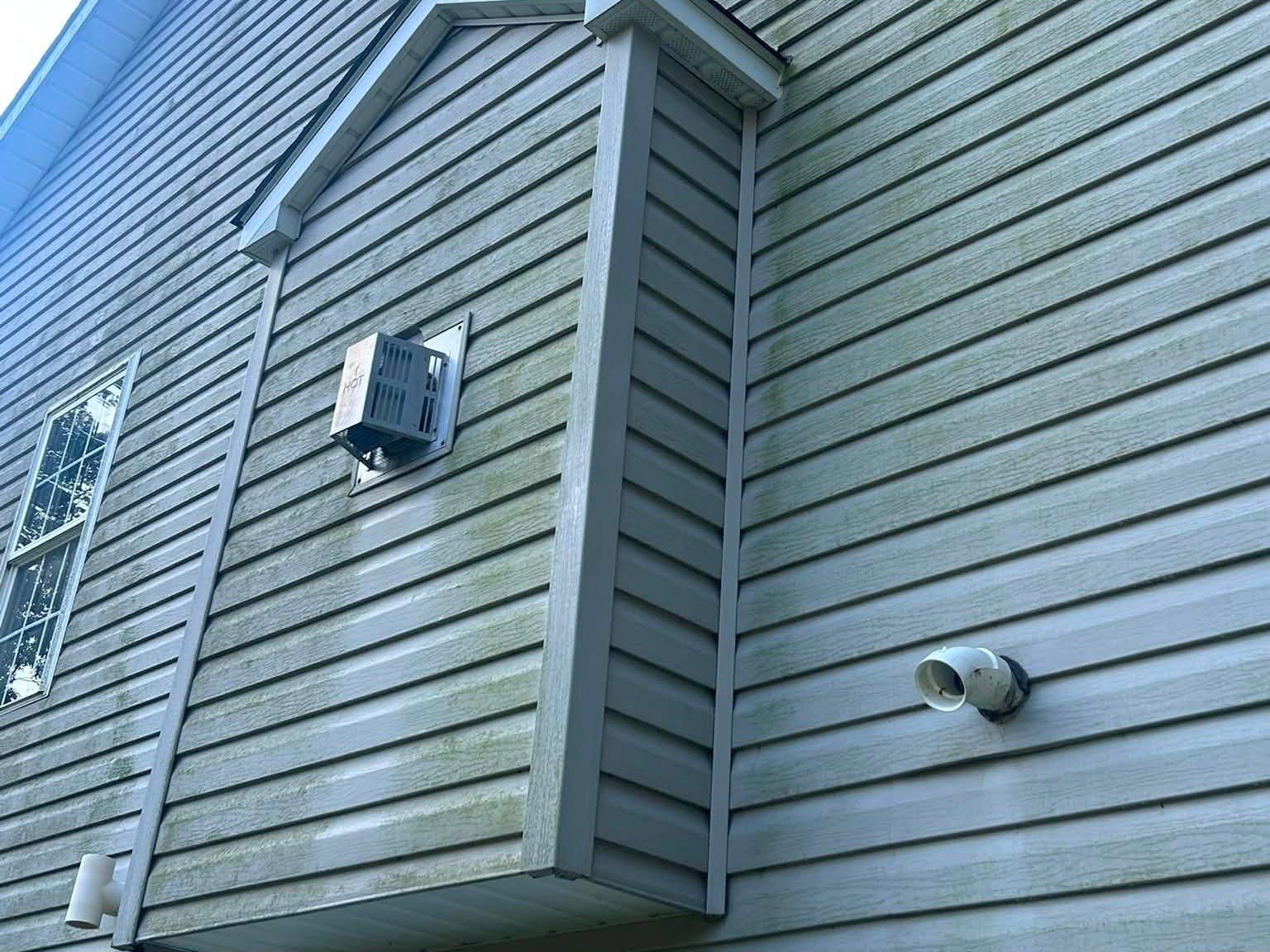 Gray vinyl siding with green algae streaks around a bump-out before soft washing