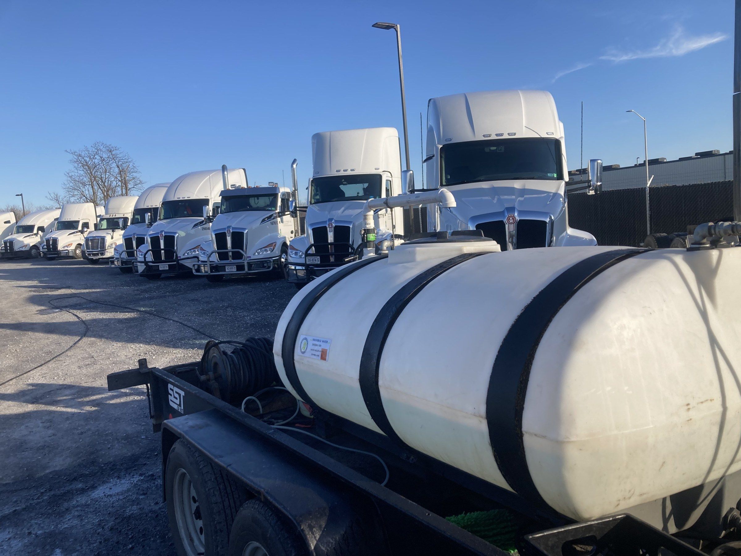 Chem-Clean water tank trailer, hose reels loaded, parked in front of a row of white semi tractors on a truck yard