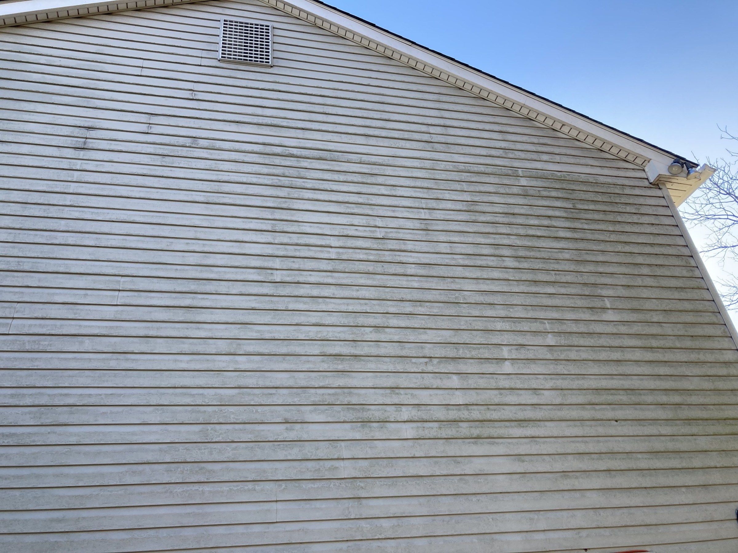 Mildew streaks running down gray vinyl siding on a gable end, just below the roof