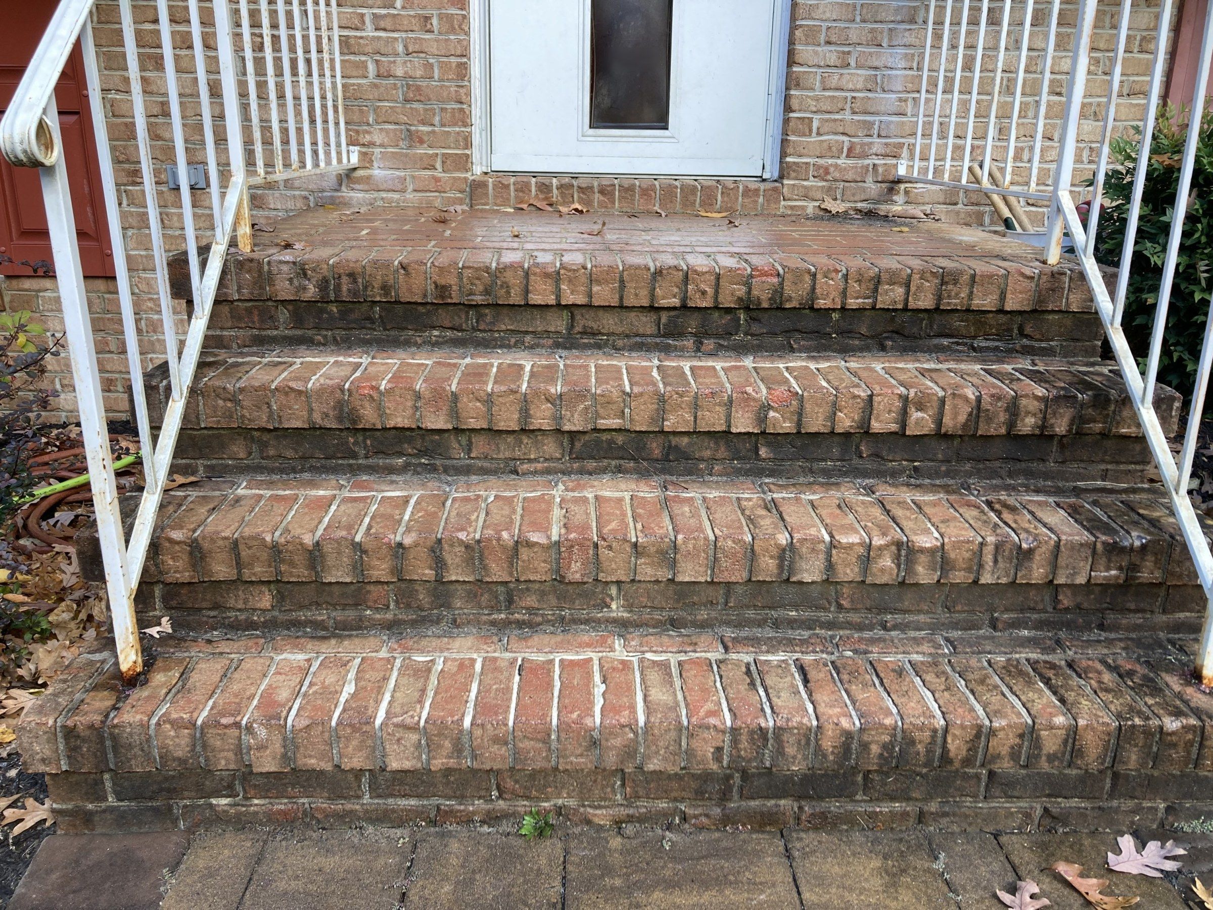 Brick front steps with white iron rails, dark with grime and fallen leaves