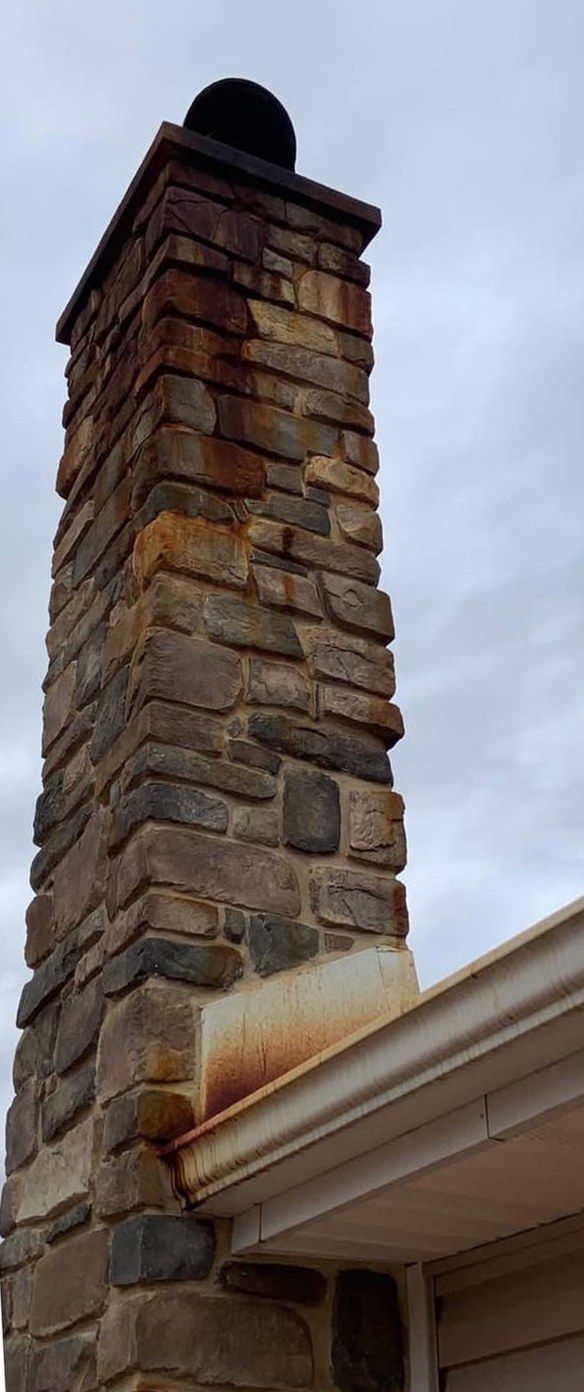 Stone chimney with orange rust streaks running down from the cap