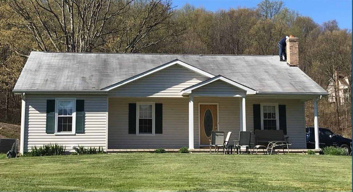 Ranch house with a streaked gray roof and dull siding, a worker on the roof